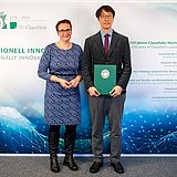 Die Tu-Präsidentin und Prof. Paek stehen vor der TU-Fotowand mit der Urkunde.